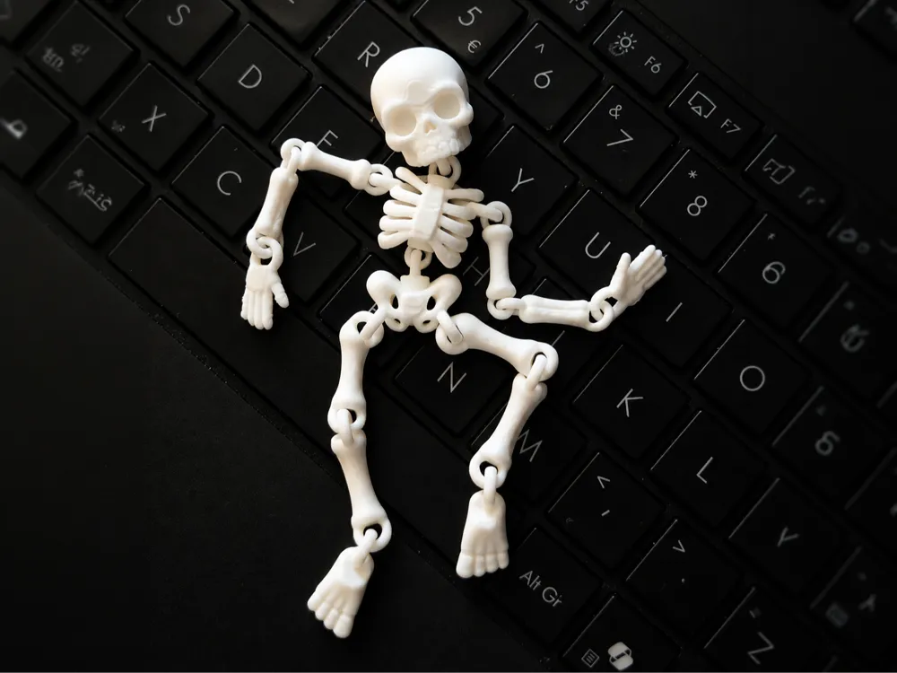 Esqueleto humano articulado flexible impreso en 3D blanco poseable sobre teclado negro