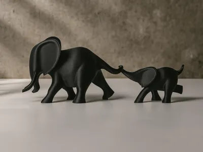 Dúo de elefantes mamá e hijo tomándose de la trompa impresos en 3D en PLA negro sobre superficie blanca