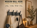 Perchero de pared 3D negro con 5 ganchos con ropa, llaves y bolso colgados en ambiente moderno
