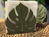 Servilletero 3D con diseño de hoja Monstera en color verde grisáceo sobre superficie clara